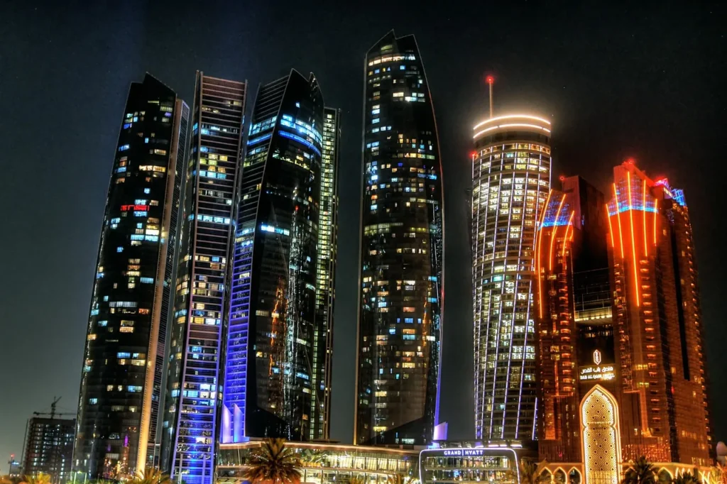 Skyscrapers in Abu Dhabi, United Arab Emirates, lit up at night with various colors, including blue, orange, and white, showcasing modern architecture.