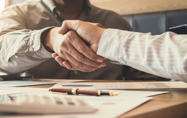 MyFastBroker.com Partnership Agreement Two professionals shaking hands over financial documents, representing a deal made through MyFastBroker.com.