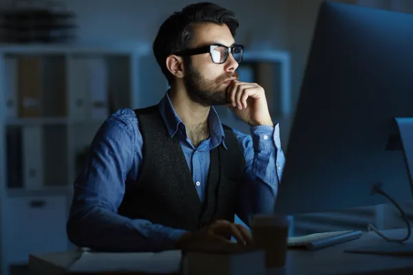 A man with glasses, possibly of Middle Eastern descent, thoughtfully working at a computer, representing users researching financial opportunities on MyFastBroker.com.