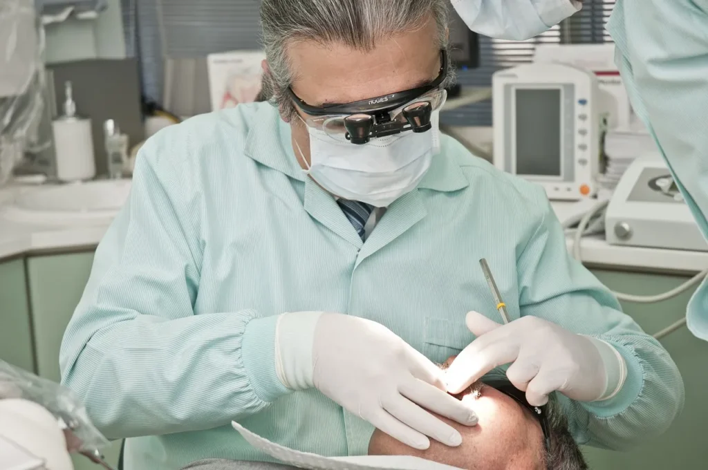 A dental professional, wearing magnifying loupes and gloves, performs a detailed examination or procedure on a patient in a dental office.
