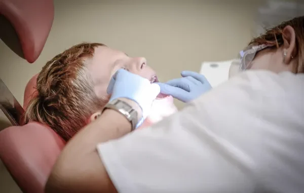 Decoding the Dental Hygienist Salary: What You Can Expect to Earn A dental hygienist wearing blue gloves examining a young patient's teeth under a bright light in a dental chair.
